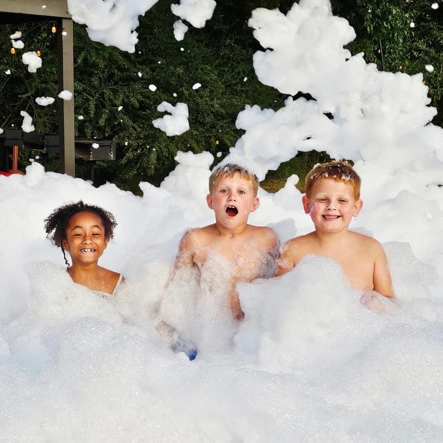 Three children joyfully play in a large pile of bubbles.