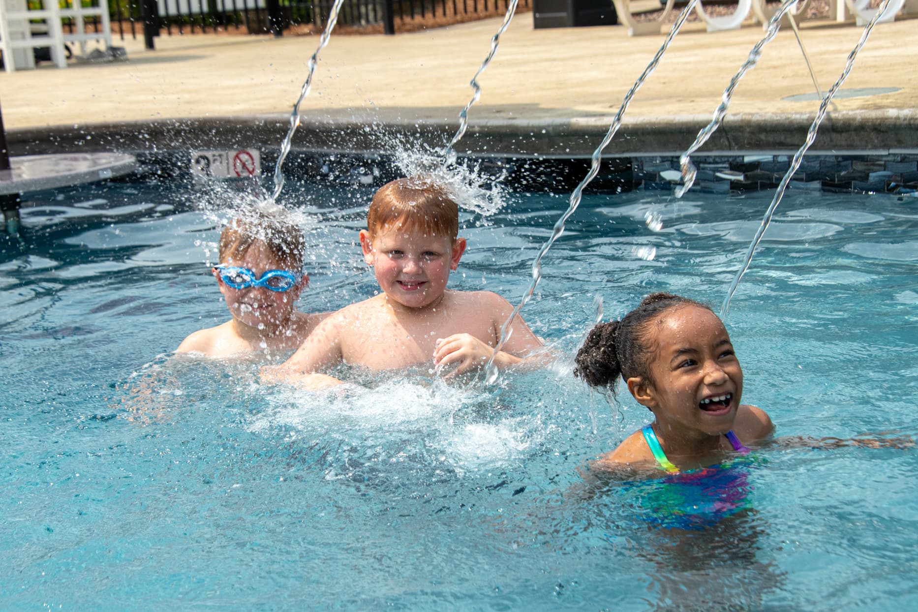 Three children play in a pool, splashing water and enjoying their time together.