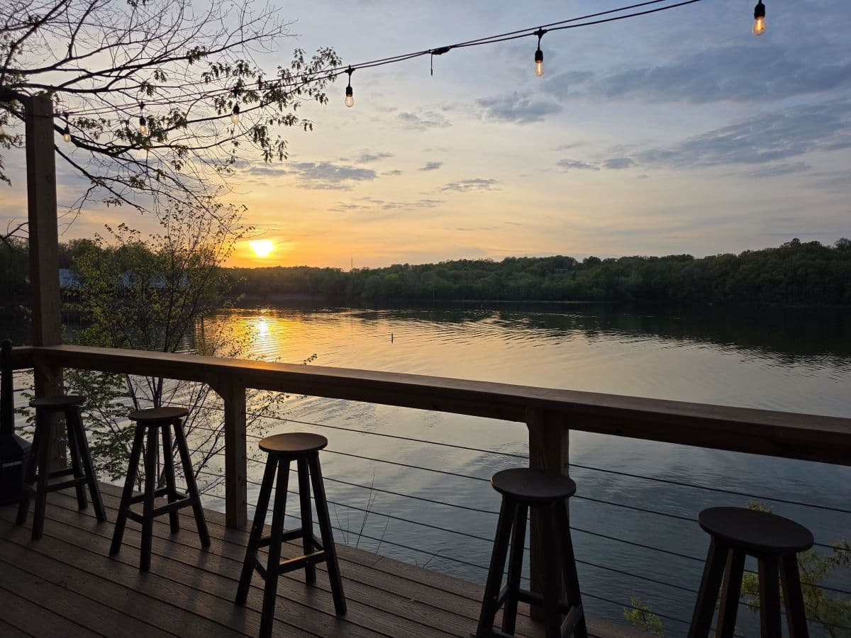 Sunset over a calm river viewed from a deck with wooden stools. Sunset over a calm river viewed from a deck with wooden stools.