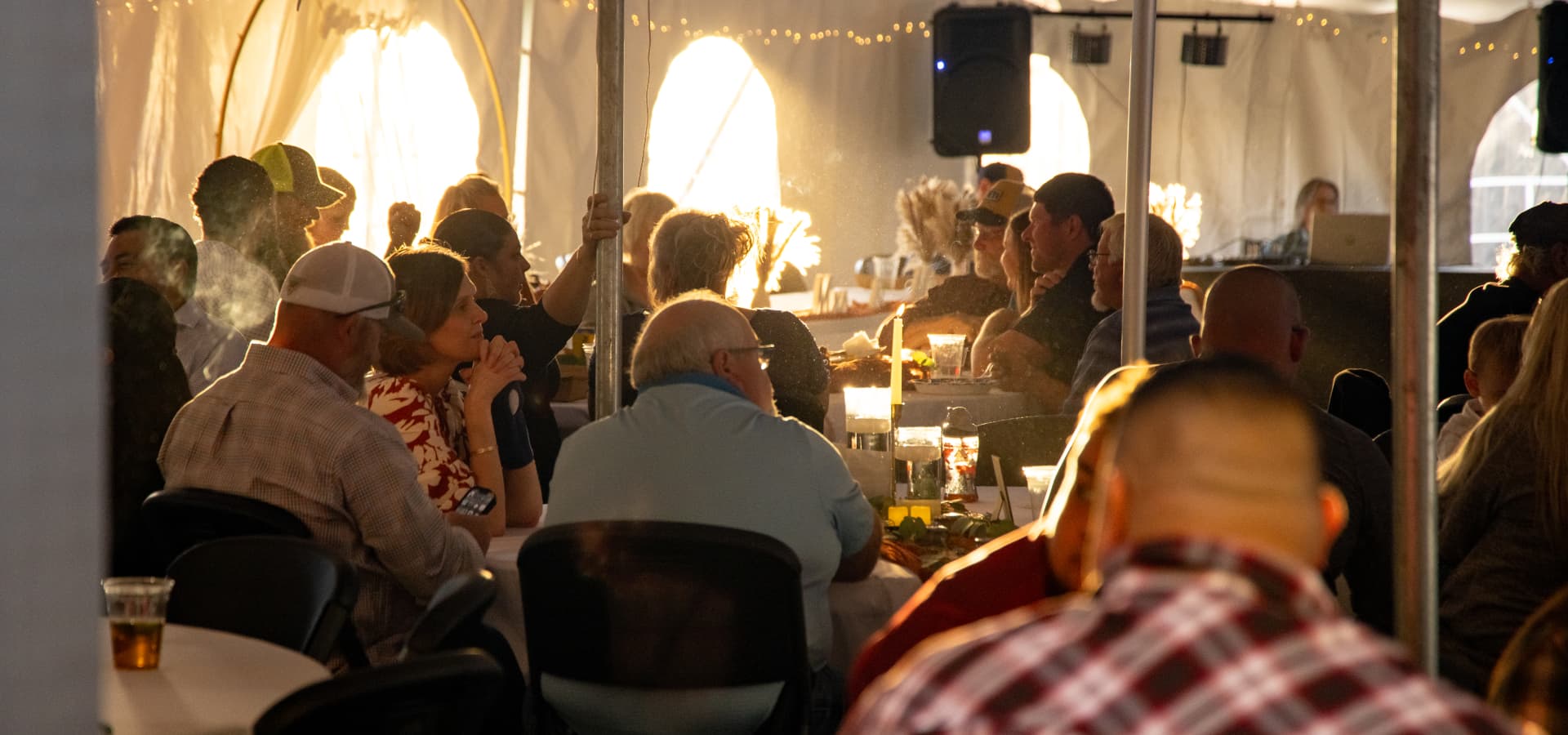 A crowd of people gathered at tables under a tent, enjoying a lively event.