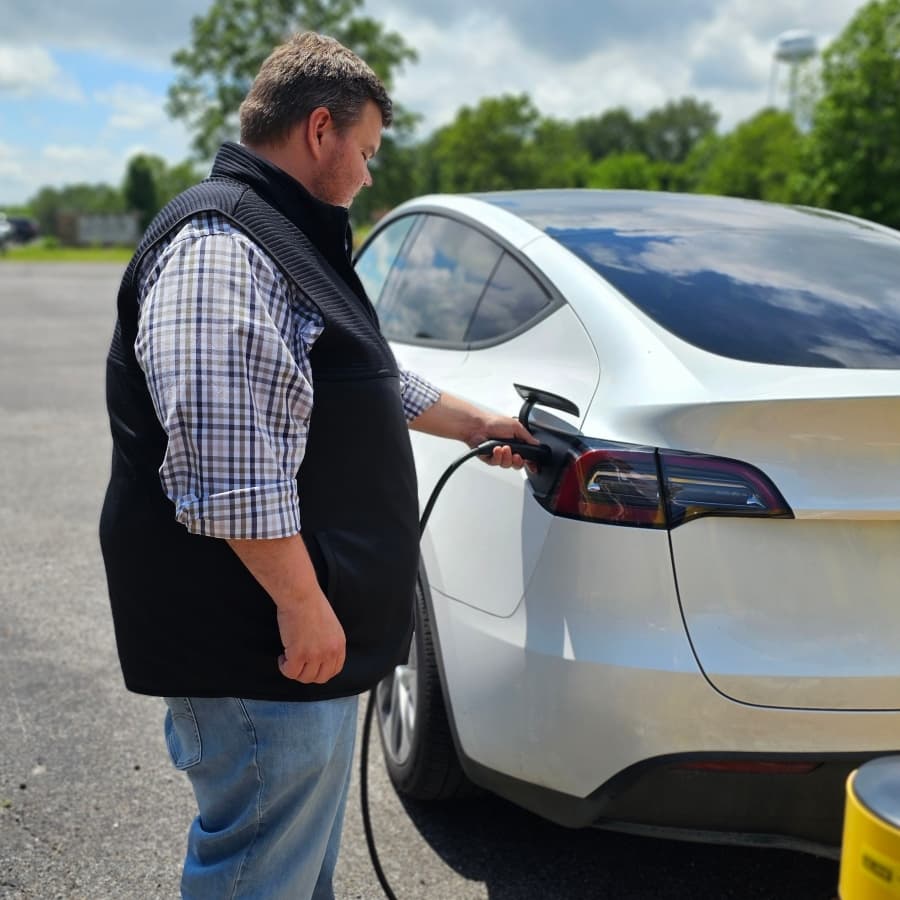 A person is charging a silver electric vehicle at a charging station.