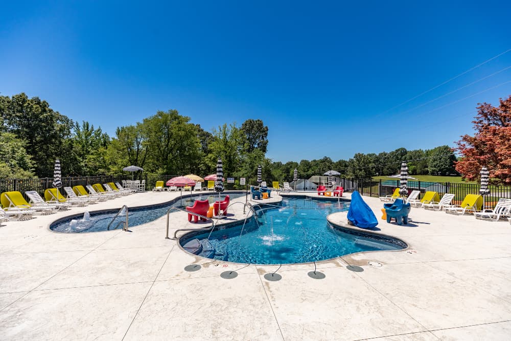 A brightly lit pool area featuring comfortable lounge chairs and vibrant umbrellas against a clear blue sky.