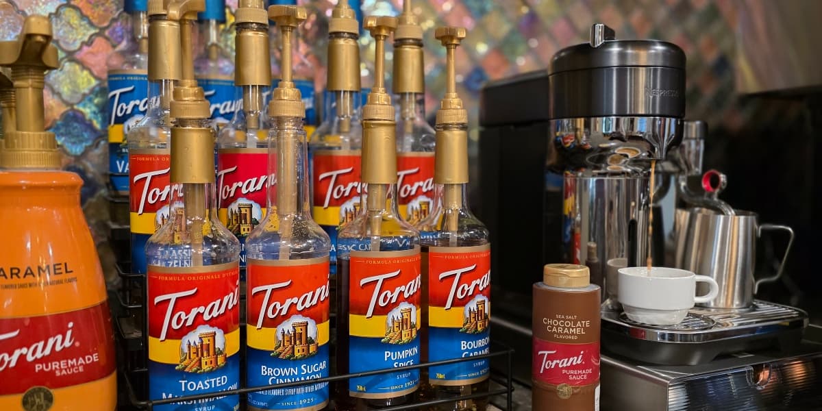 A display of Torani flavored syrup bottles next to an espresso machine and a coffee cup.