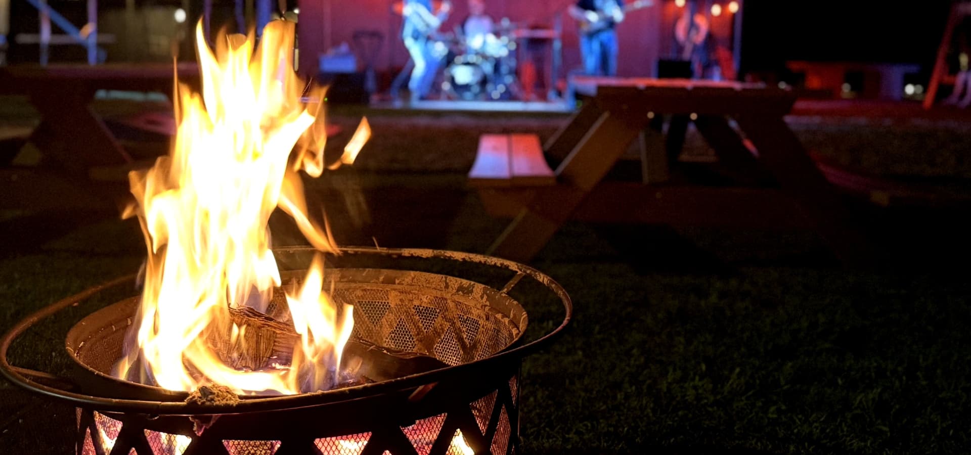 A glowing campfire in the foreground with a live band performing on stage in the background.
