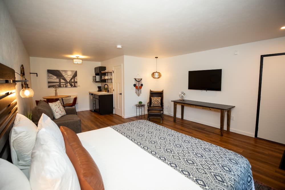 Modern studio interior featuring a bed, kitchenette, seating area, and wall-mounted TV.