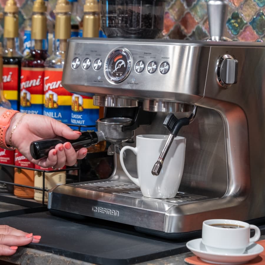 A person is preparing espresso using a coffee machine with a white cup underneath the spout.
