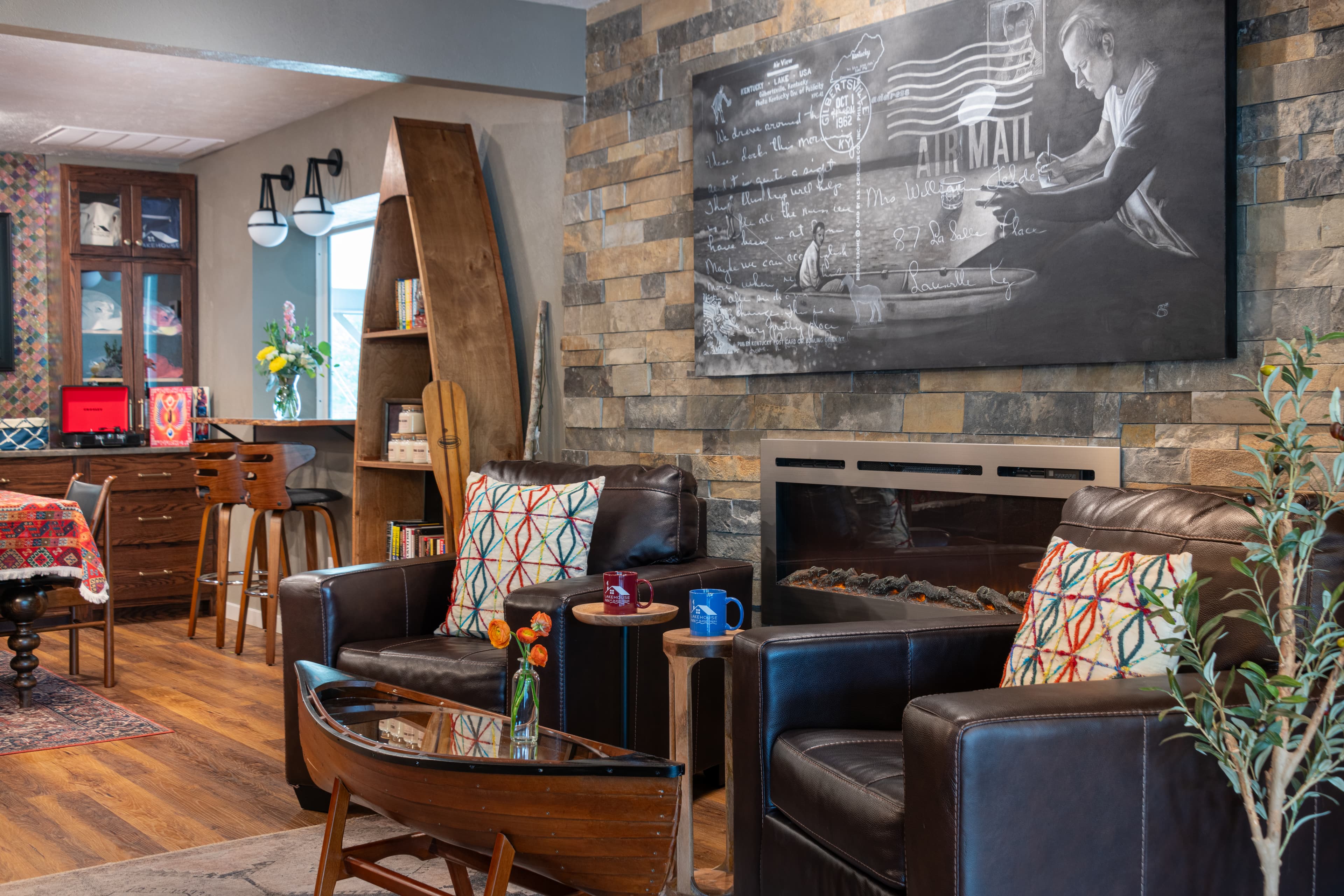 A cozy living room features two leather armchairs, a glass coffee table, and a stone wall with an artwork depicting air mail.