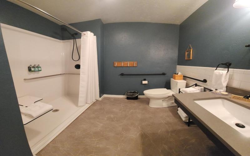 large private bath with walk in shower, toilet with grab bars, accessible sink vanity