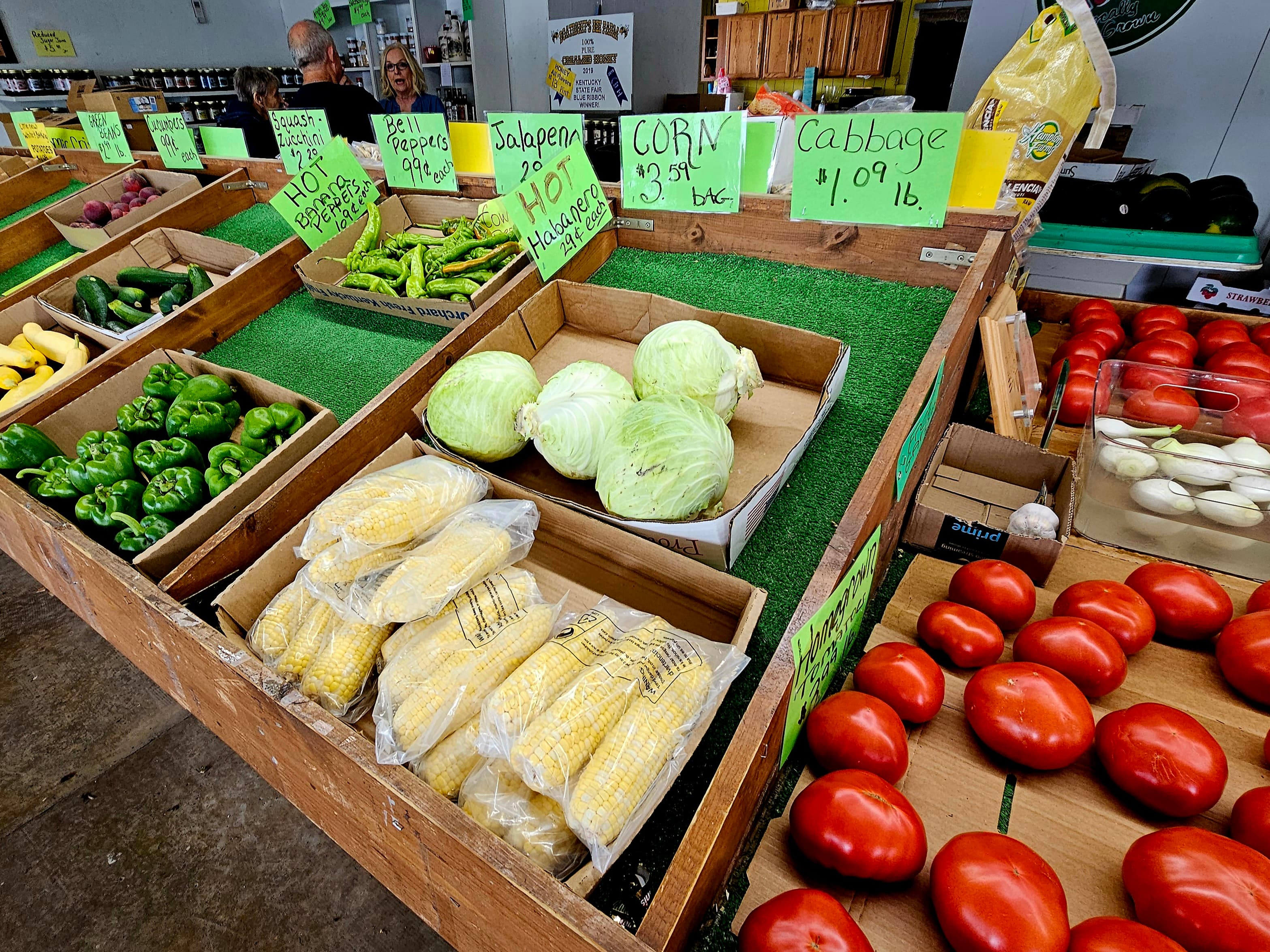 A display of fresh vegetables including corn, cabbage, and various peppers at a market.