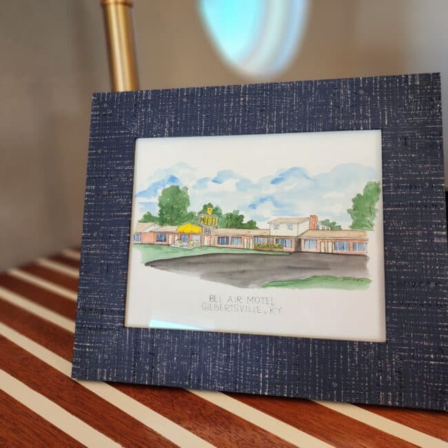 A watercolor painting of the Bel Air Motel in Gilbertsville, KY, displayed in a textured blue frame. A watercolor painting of the Bel Air Motel in Gilbertsville, KY, displayed in a textured blue frame.