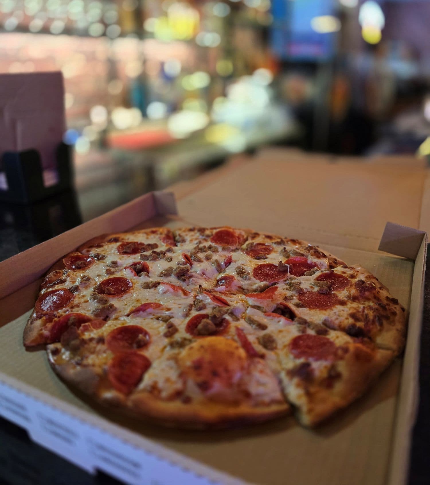 A freshly baked pepperoni and sausage pizza in an open delivery box.