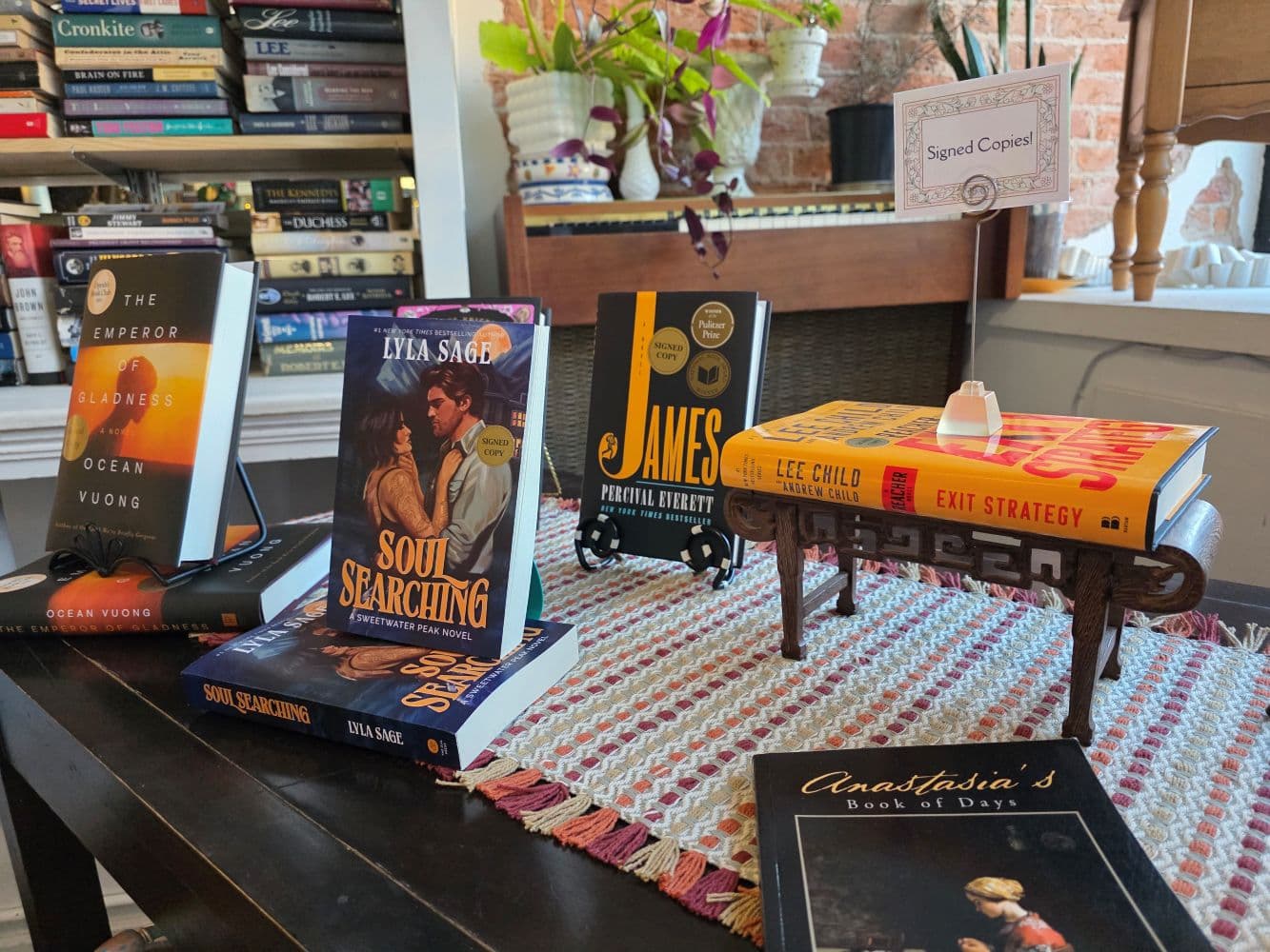 A cozy display of books on a table, including titles like "Soul Searching" and "Exit Strategy," with a sign for signed copies.
