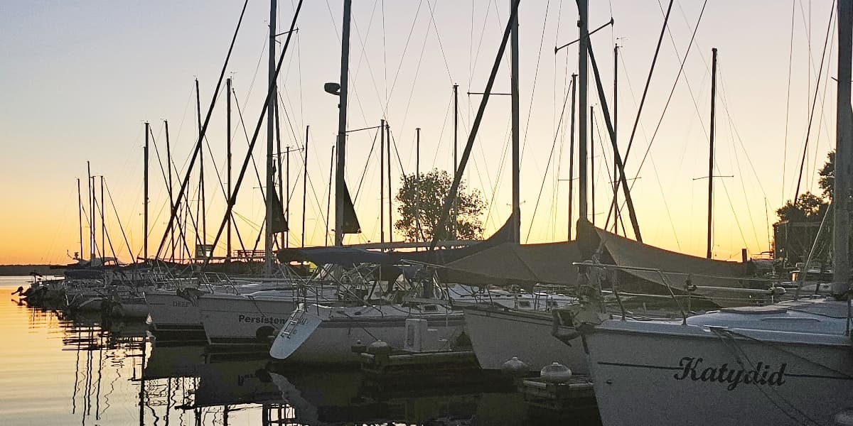 A peaceful marina at sunset, lined with sailboats and reflections on the water.