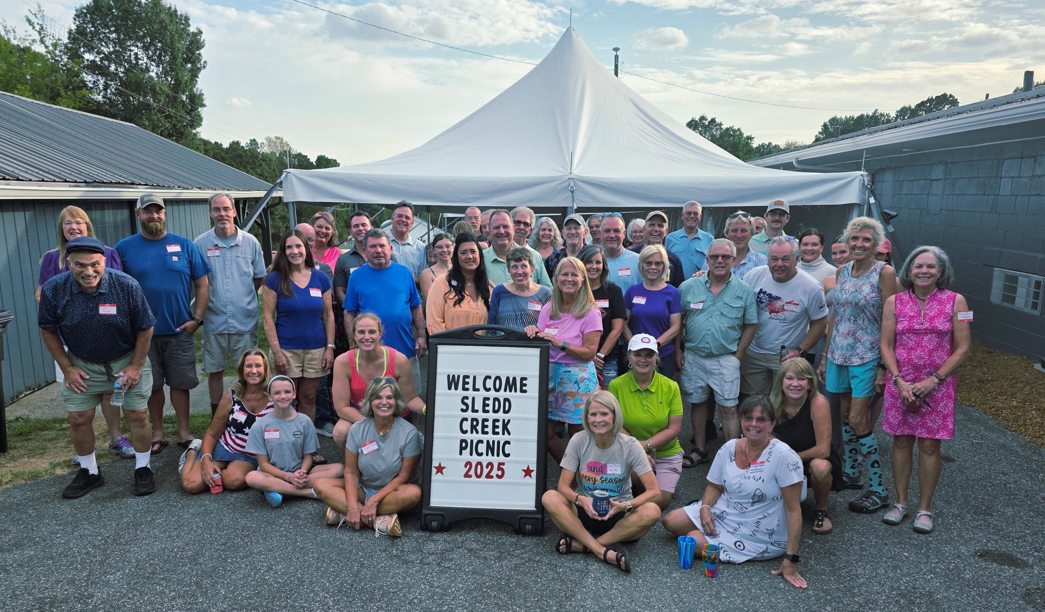 A large group of people gathers for the Sled Creek Picnic 2025, posing in front of a welcome sign.