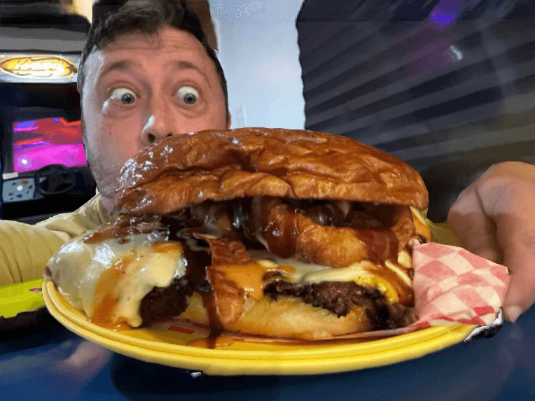 A surprised man holds up a large, decadent burger with cheese and bacon. A surprised man holds up a large, decadent burger with cheese and bacon.