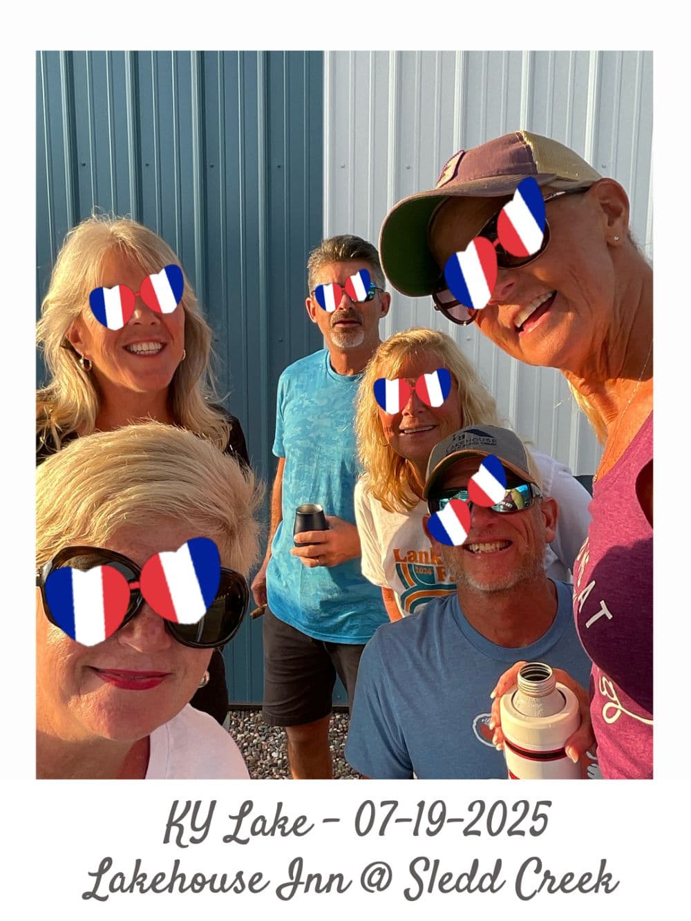 A group of six friends poses for a selfie by a lake, all wearing sunglasses with French flag designs.