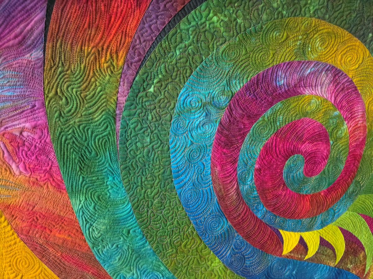 A vibrant, multicolored spiral quilt pattern with intricate stitching.
