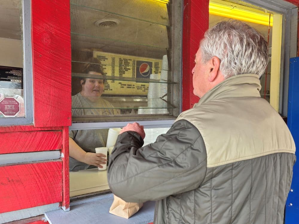 A customer interacts with a server at a window of a food stand.