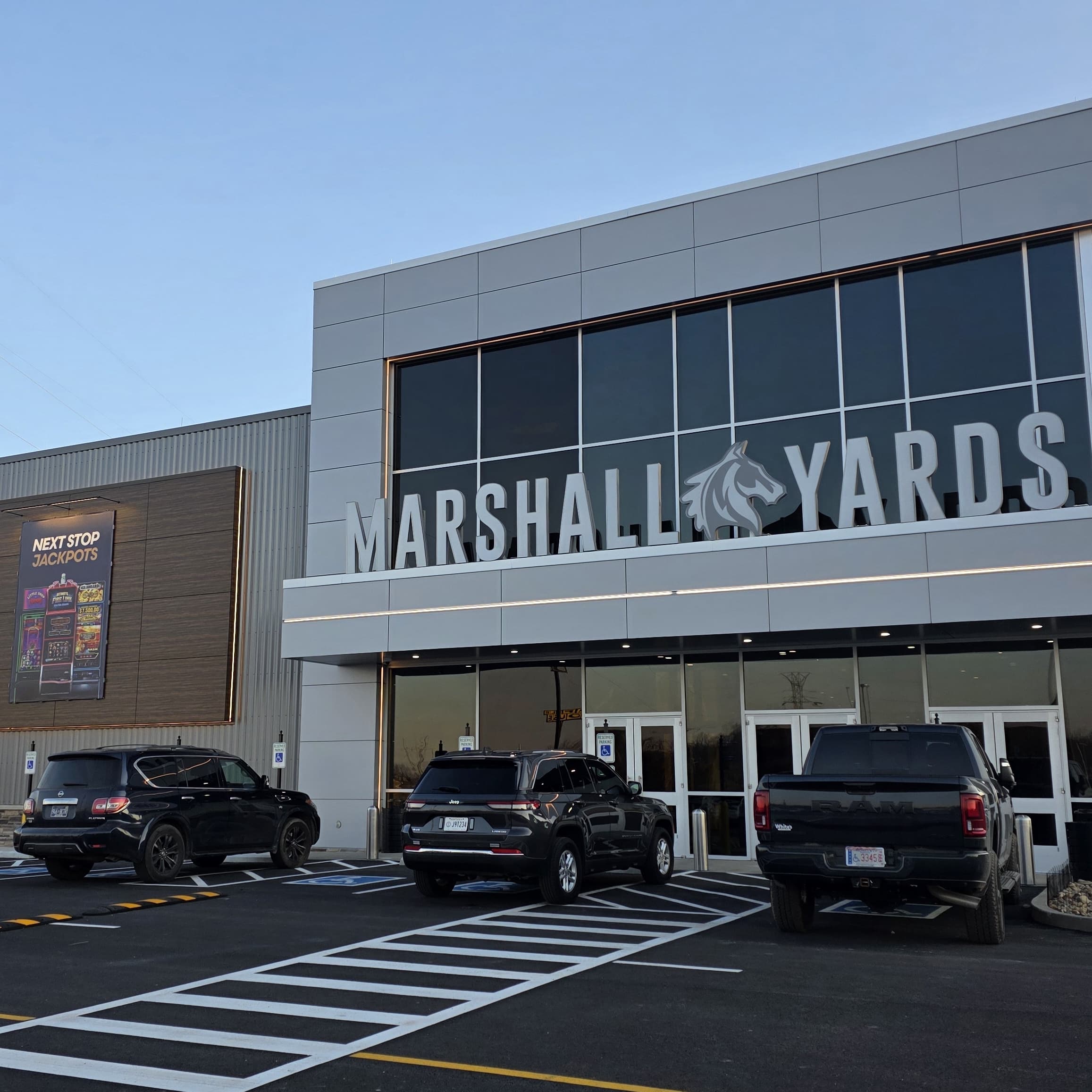 The entrance of Marshall Yards, featuring large glass windows and parked vehicles in front.