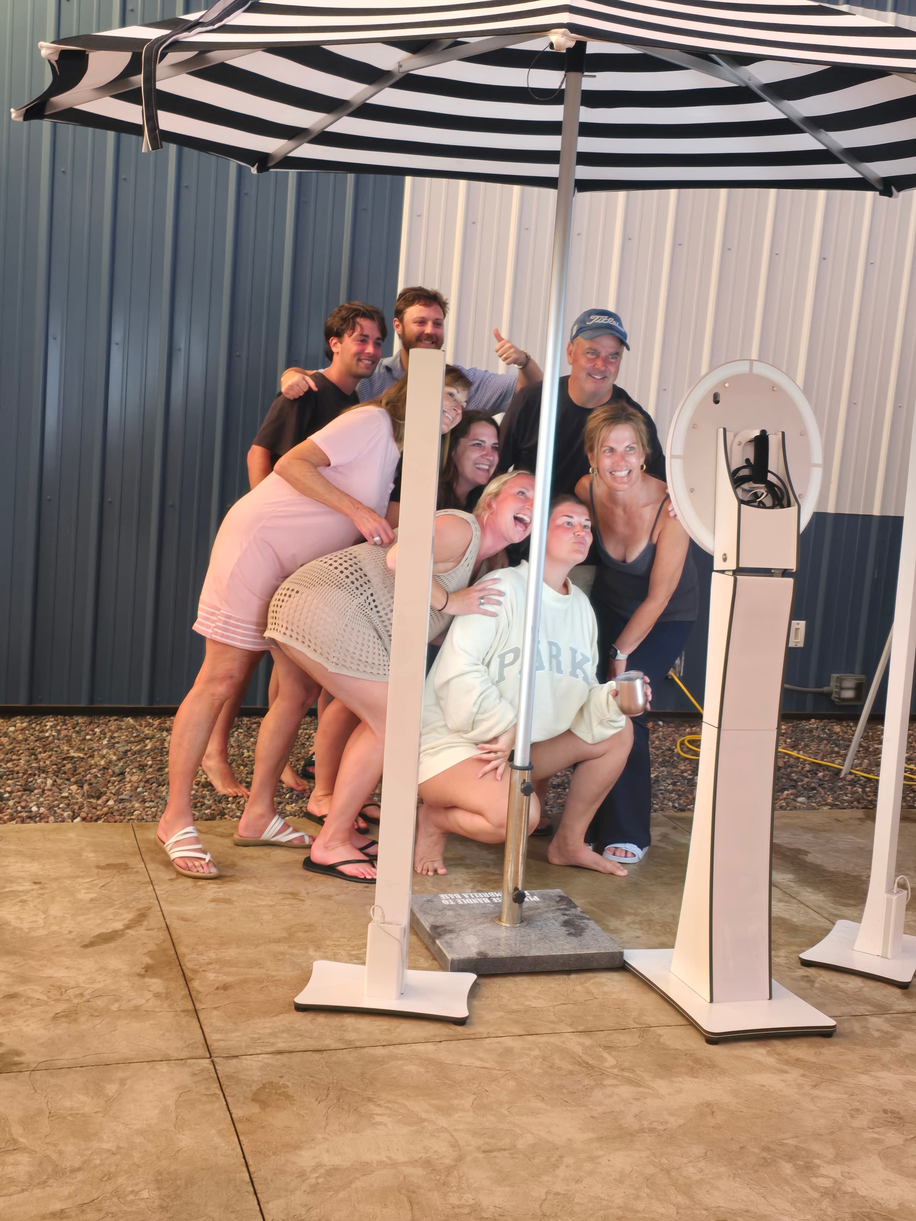 A group of friends smiling and posing together under a striped umbrella.