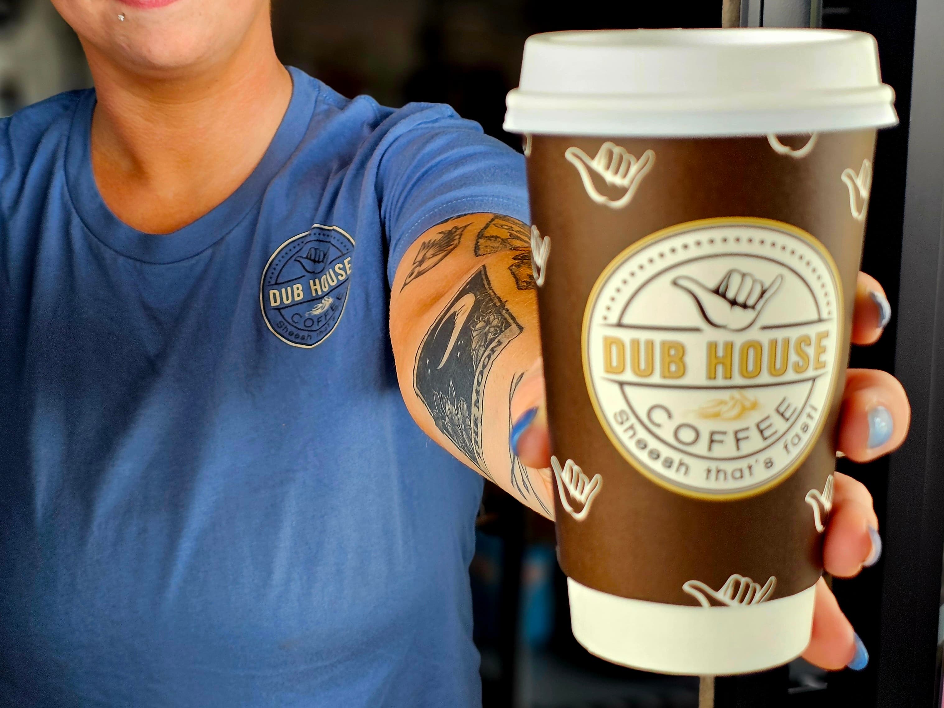 A person wearing a blue shirt with a "Dub House Coffee" logo holds out a coffee cup.