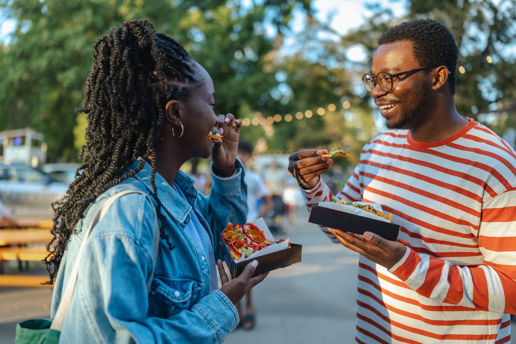 A smiling man and woman enjoy street food together at an outdoor event.