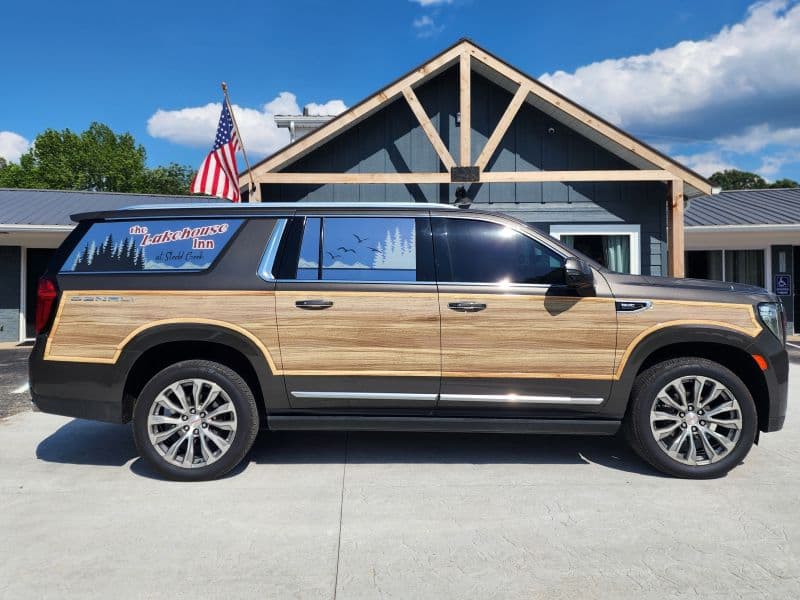 A black SUV with wood paneling parked in front of a rustic inn featuring an American flag and scenic mountain background.