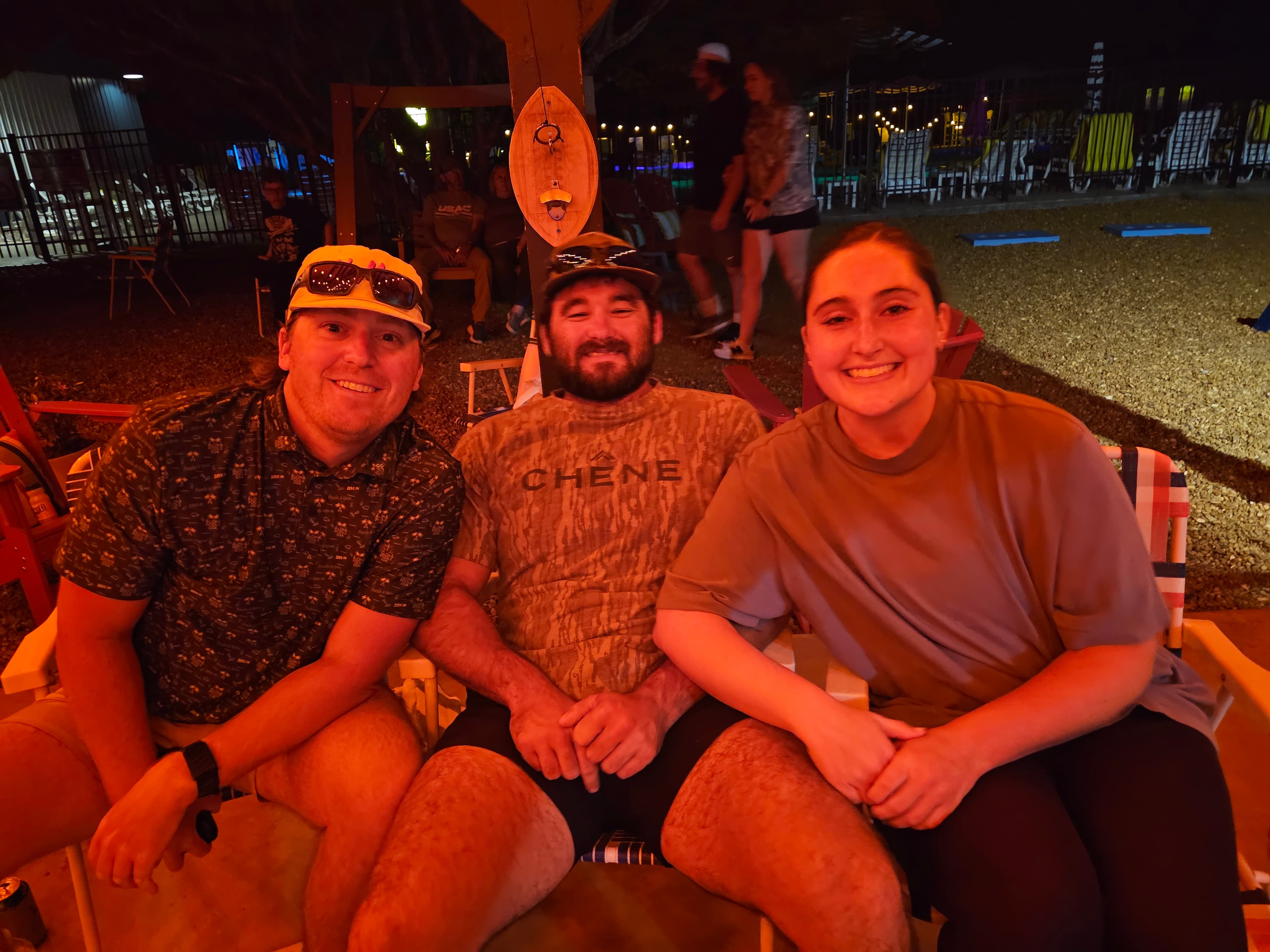 Three friends sitting together in a colorful outdoor space at night, smiling.