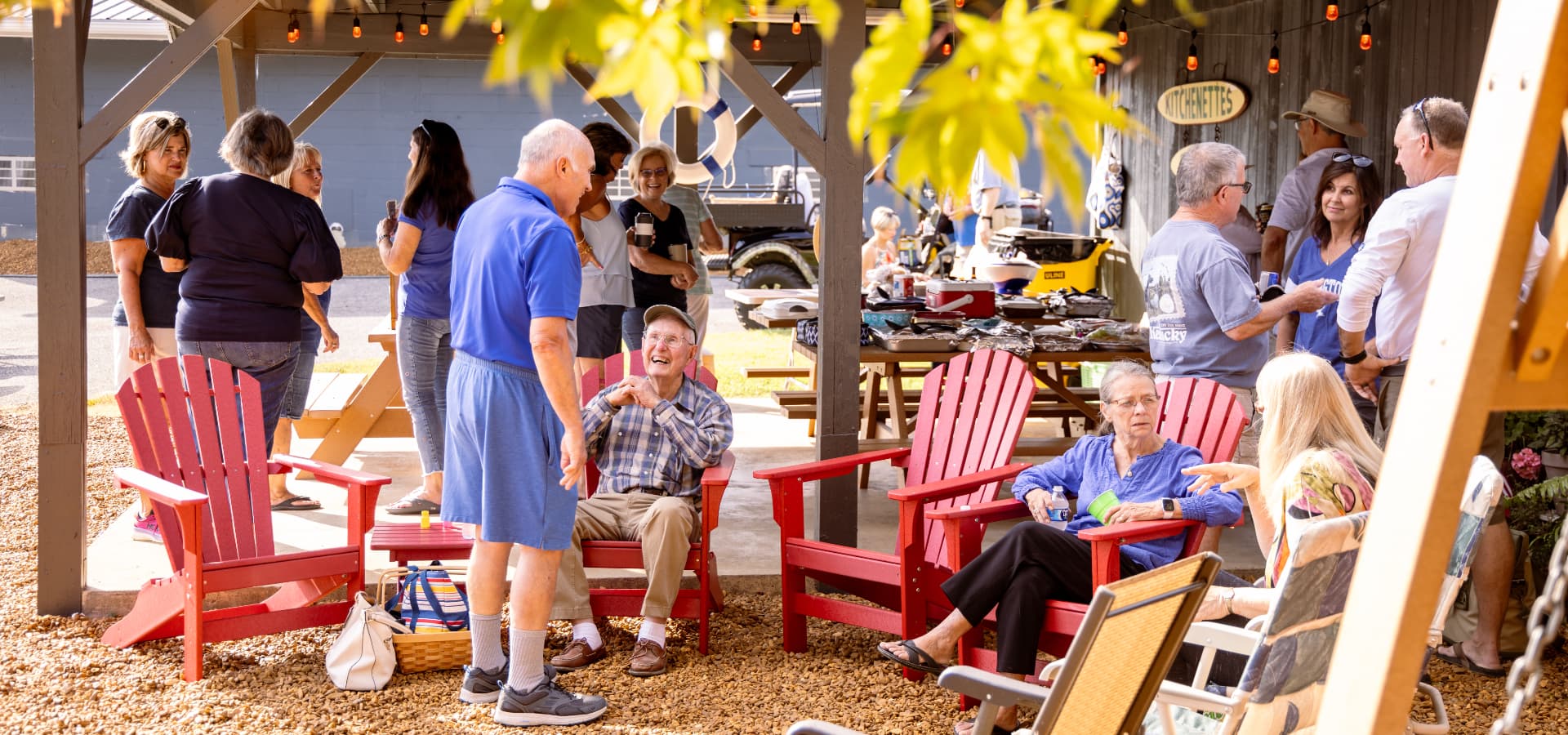 Outdoor gathering with people chatting and enjoying the setting around red Adirondack chairs.