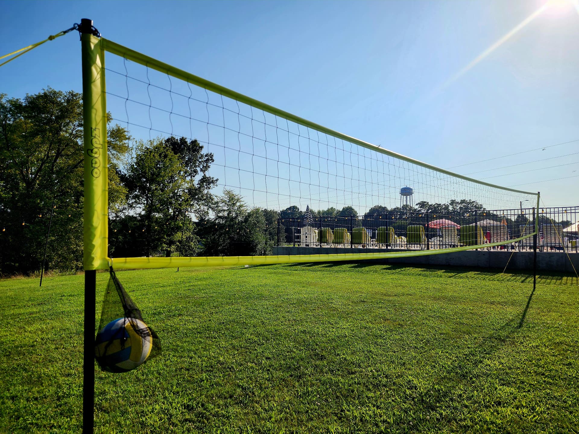A brightly colored volleyball net stands on a grassy field with a ball hanging from it under a clear sky.