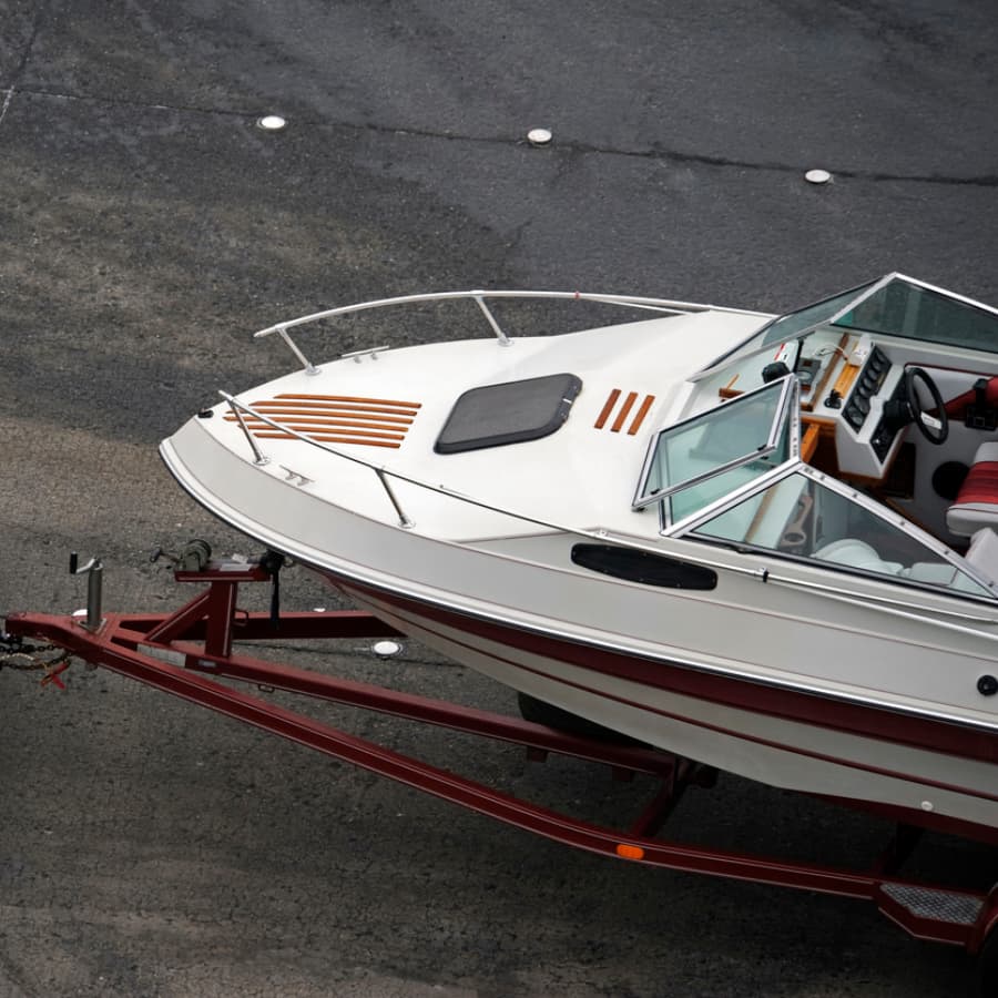 A white boat on a trailer parked on a gravel surface.