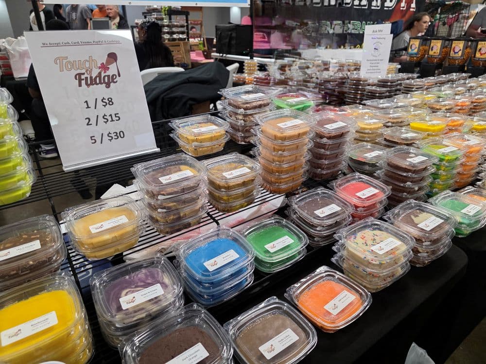 A display of colorful fudge samples in plastic containers with pricing signs at a market stall.