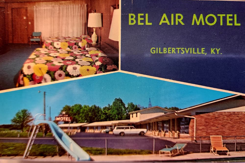 A vintage postcard featuring the Bel Air Motel in Gilbertsville, Kentucky, showing a floral-patterned bed and an outdoor view with a slide and lounging area.