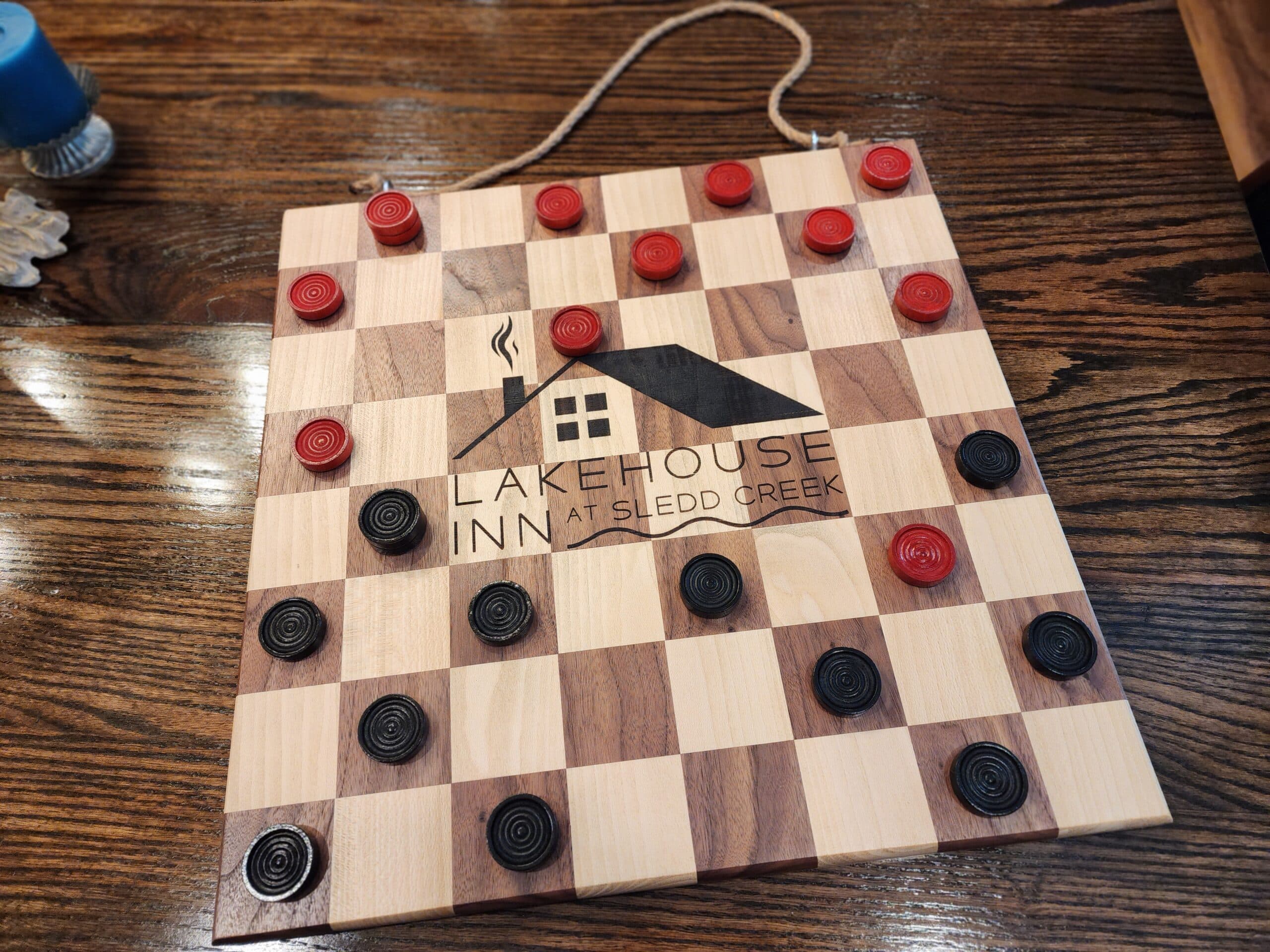 A wooden checkerboard with red and black pieces, branded with "Lakehouse Inn at Sledd Creek." A wooden checkerboard with red and black pieces, branded with "Lakehouse Inn at Sledd Creek."
