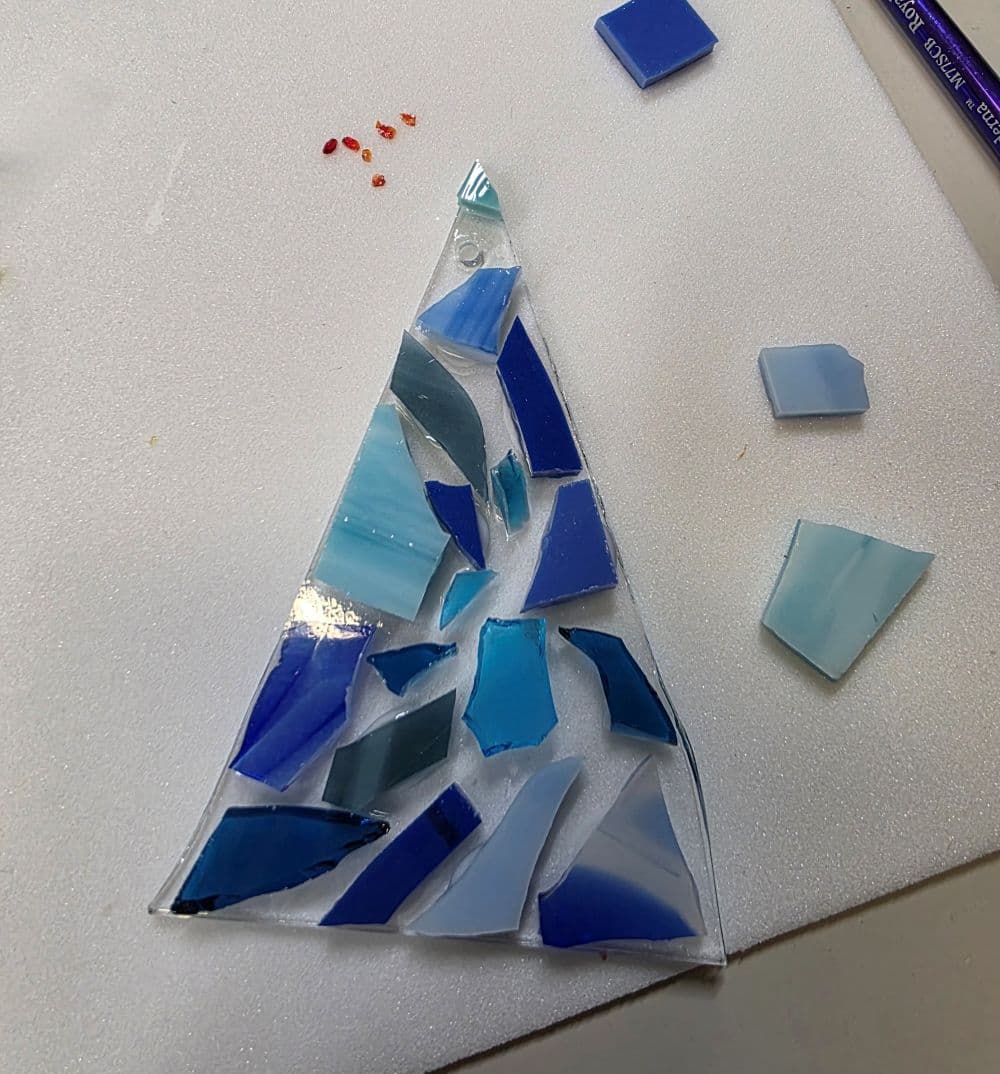 A triangular mosaic piece made of various shades of blue glass, surrounded by loose glass fragments.