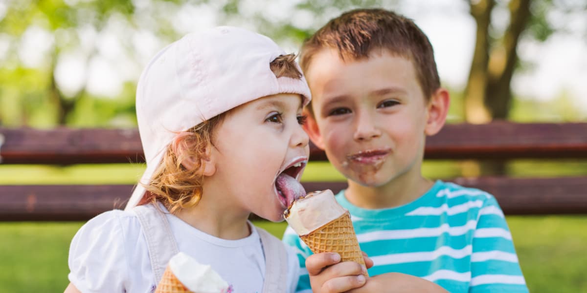 Two children enjoying ice cream on a sunny day in a park.