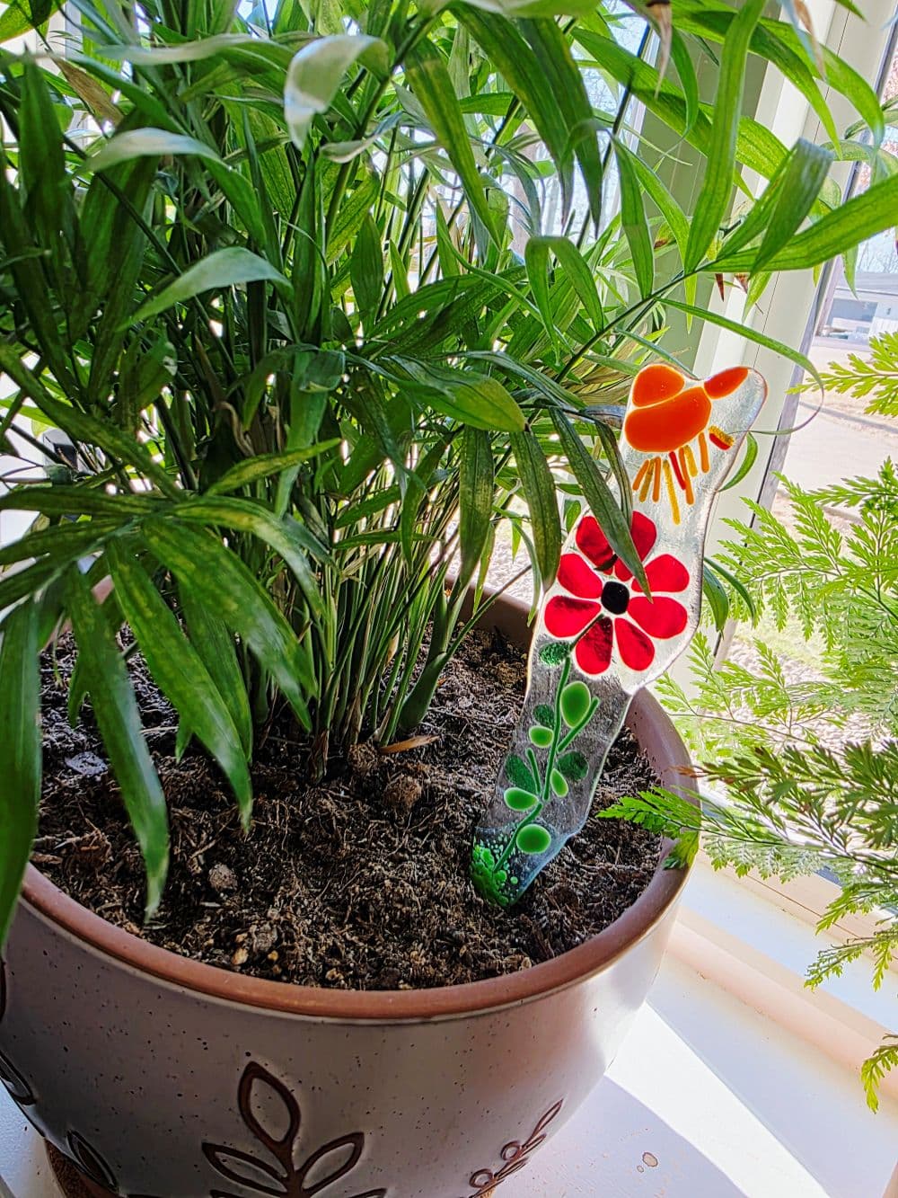 Colorful flower markers are placed among green leaves in a potted plant.