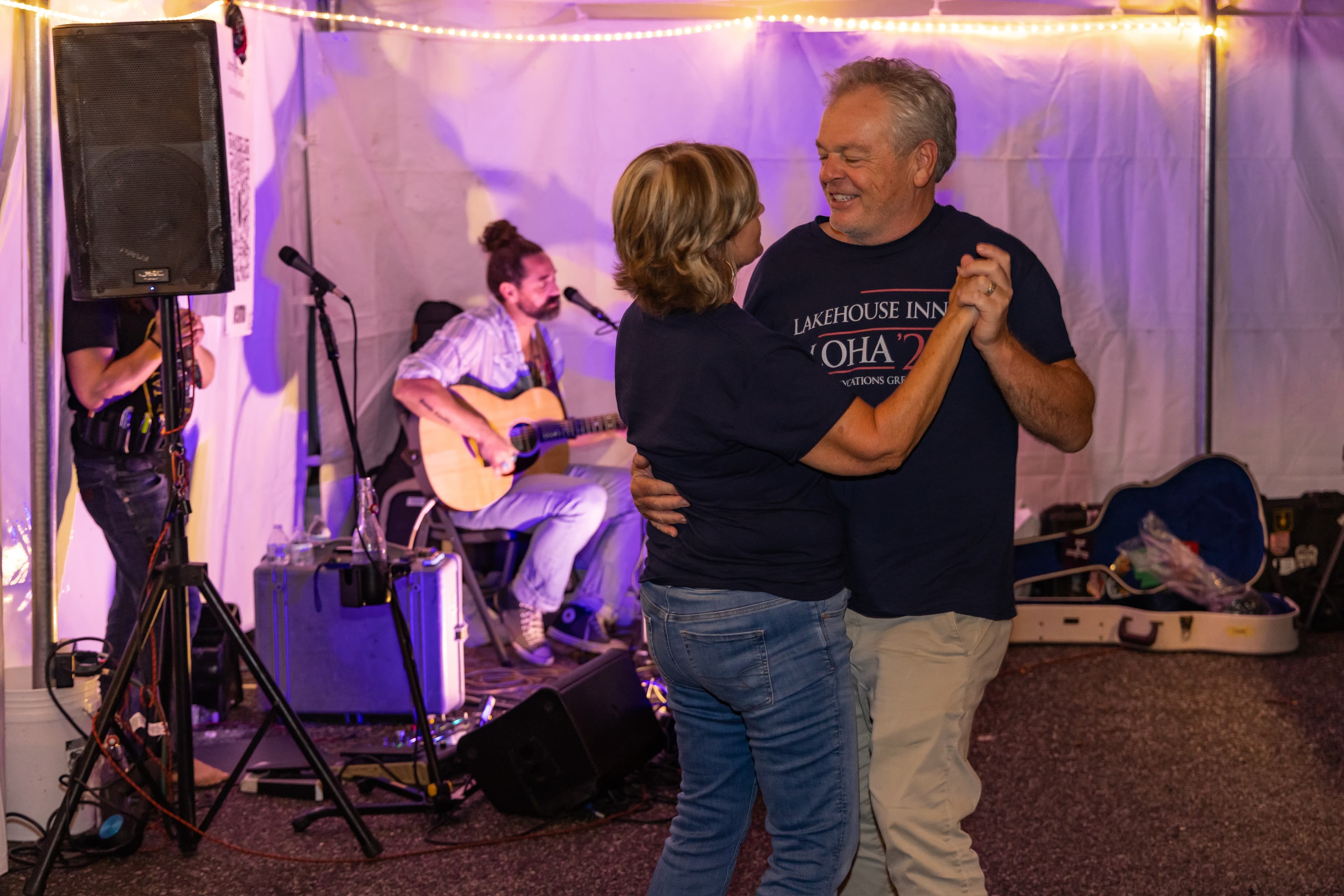 A couple dances together in front of a live musician at a tented event.
