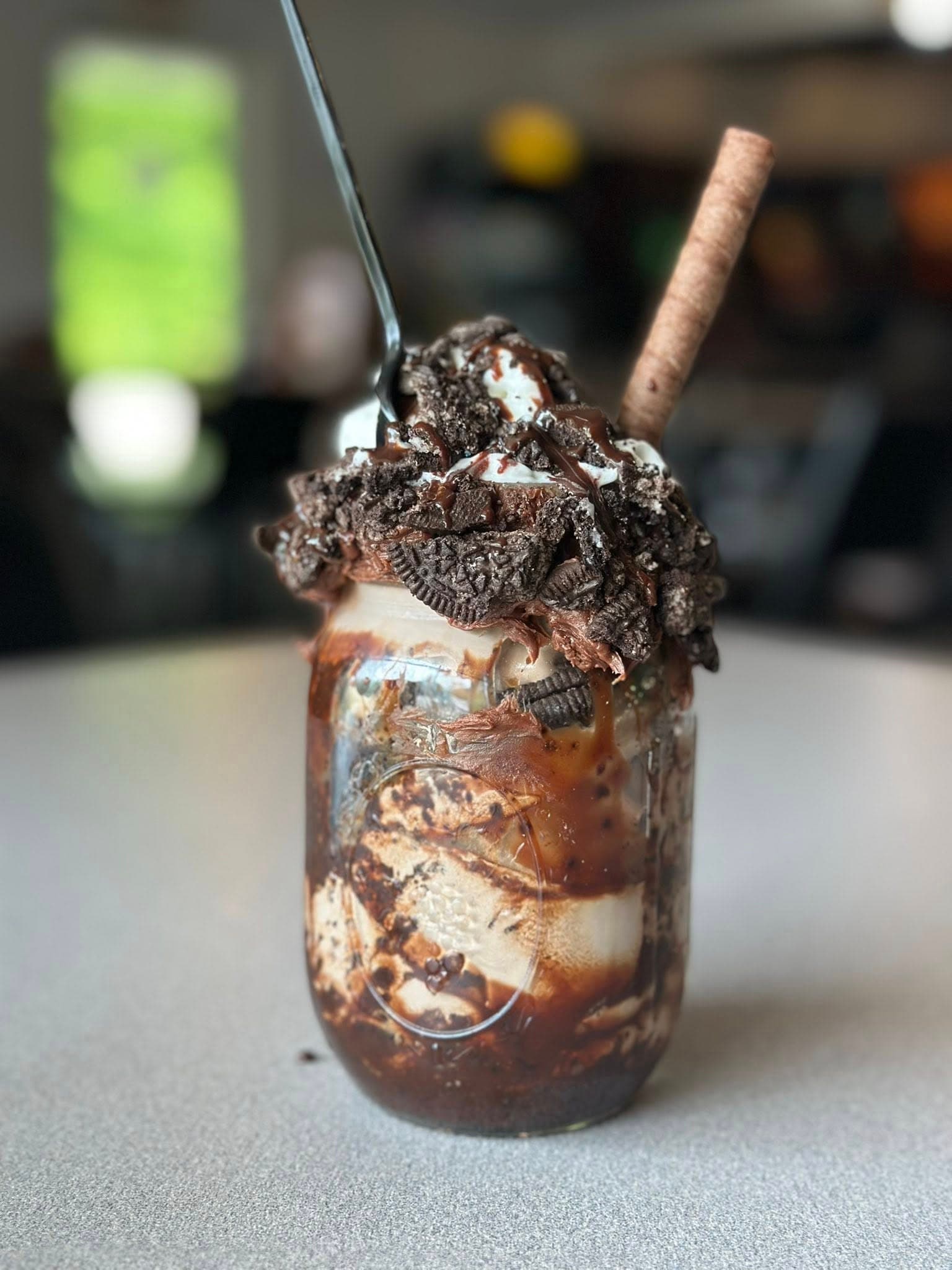 A mason jar filled with ice cream, chocolate sauce, whipped cream, crumbled cookies, and a chocolate stick.