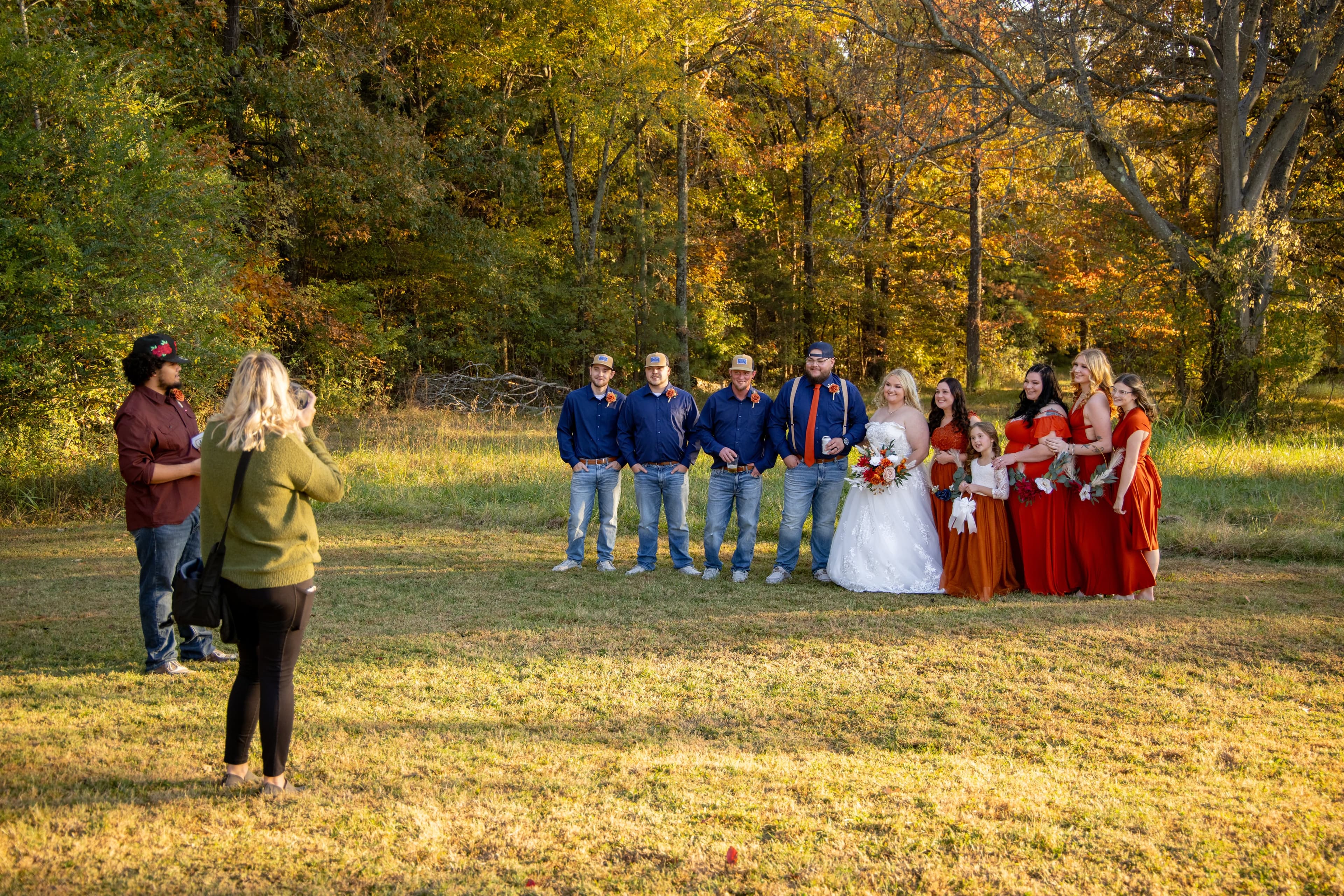 A bride poses with her wedding party in a scenic outdoor setting during autumn.