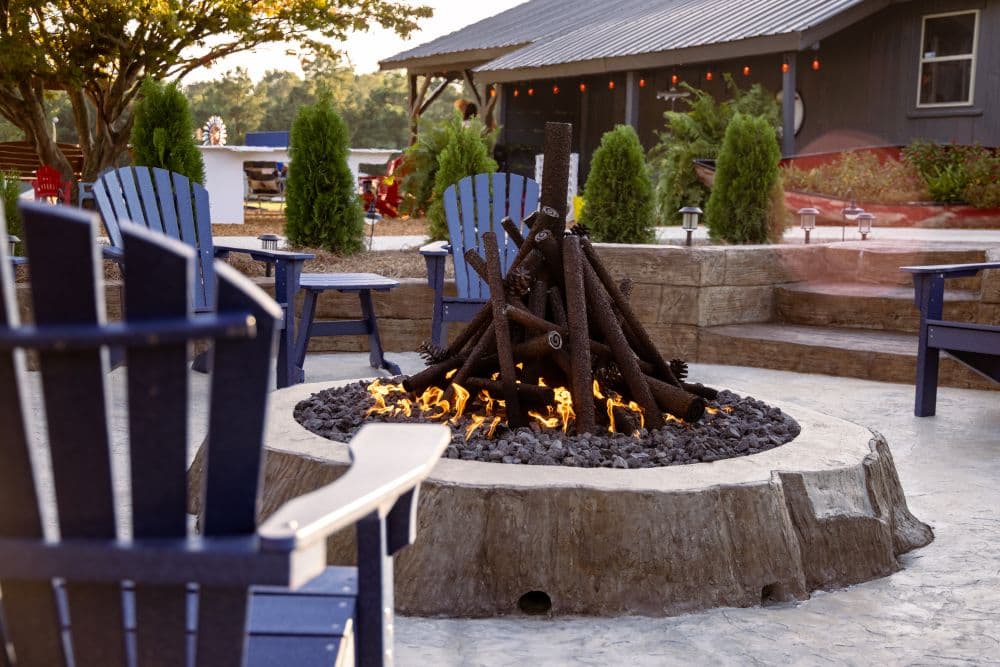 A cozy fire pit surrounded by blue chairs and greenery.