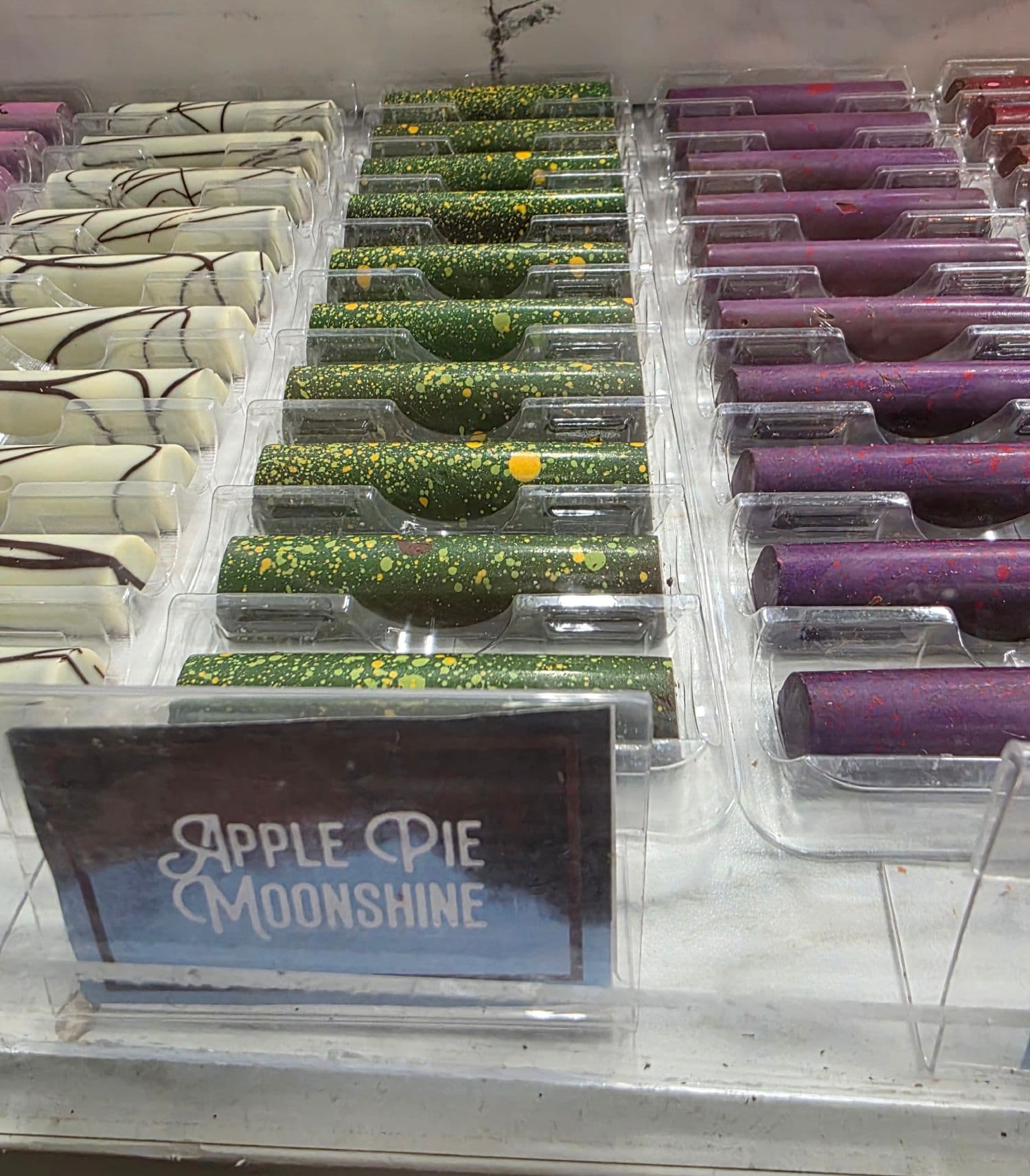A display of colorful candy tubes labeled "Apple Pie Moonshine" in various flavors and designs.