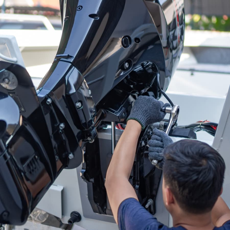 A person in gloves repairs an outboard motor.