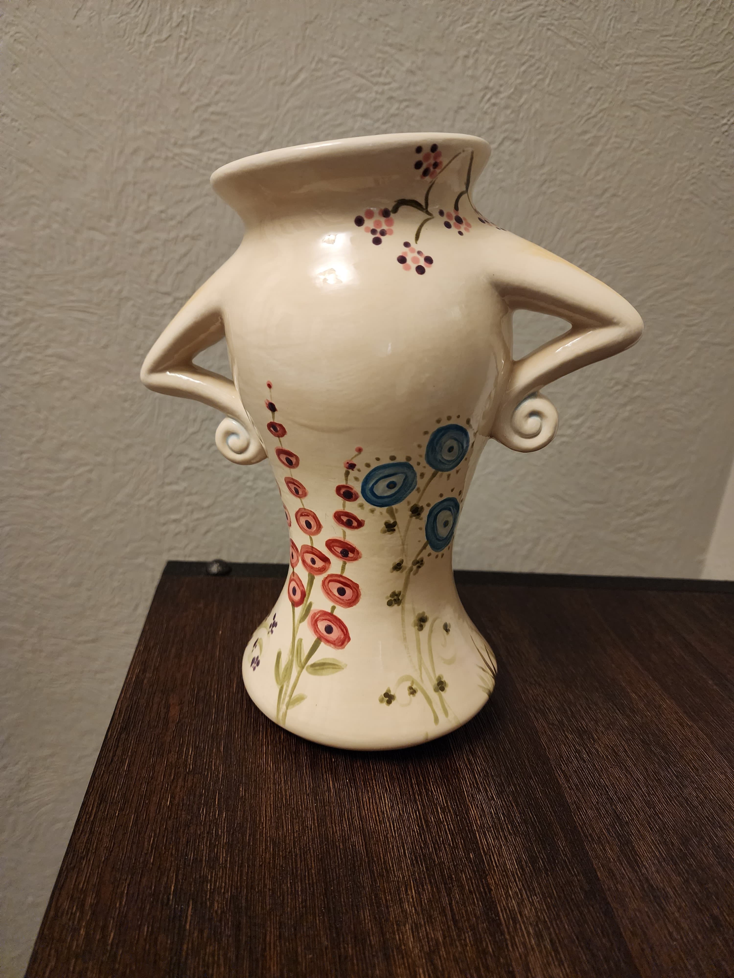 A decorative white vase with colorful floral designs and spiral handles.