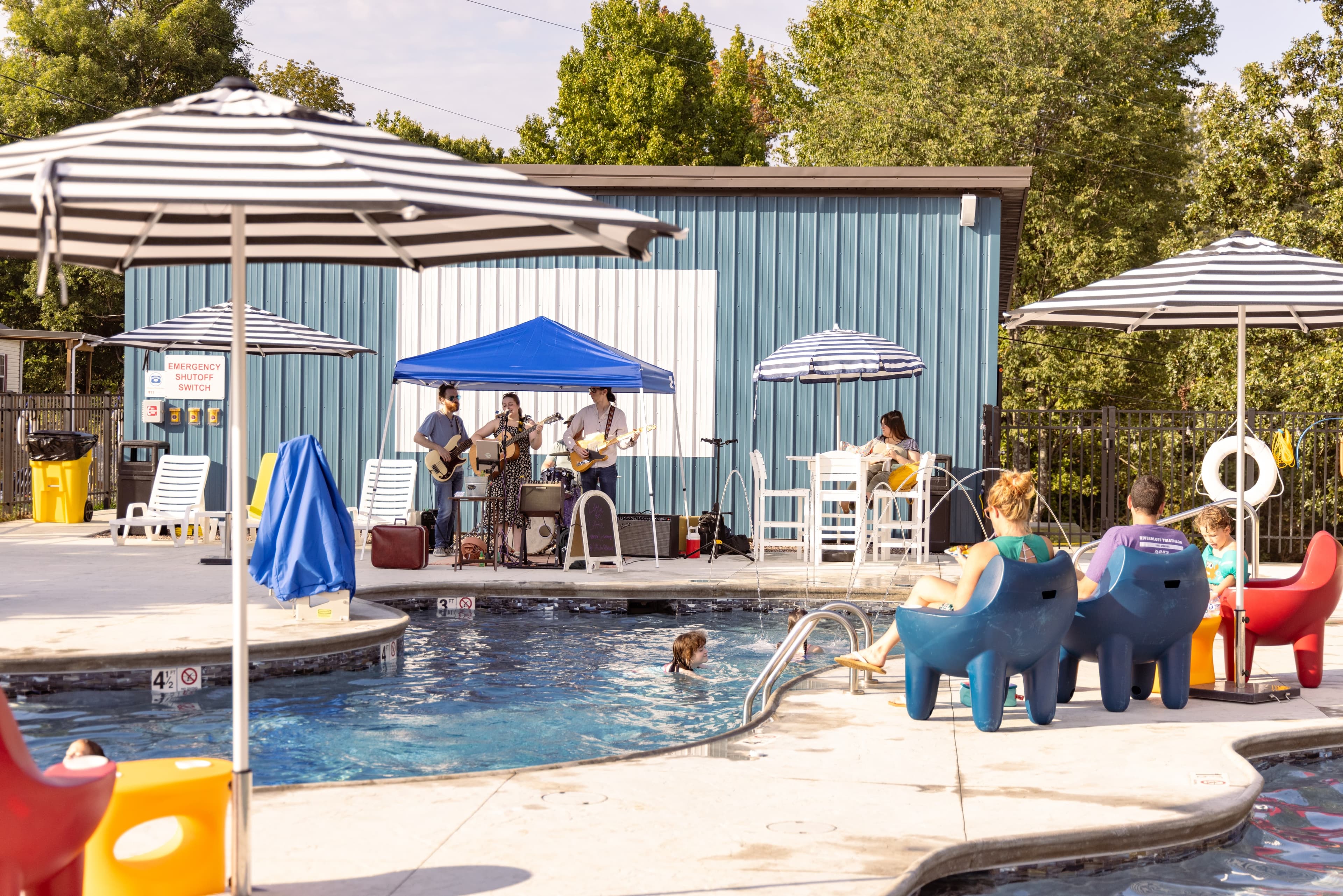 A poolside band performs under a blue tent while guests relax nearby in colorful chairs.