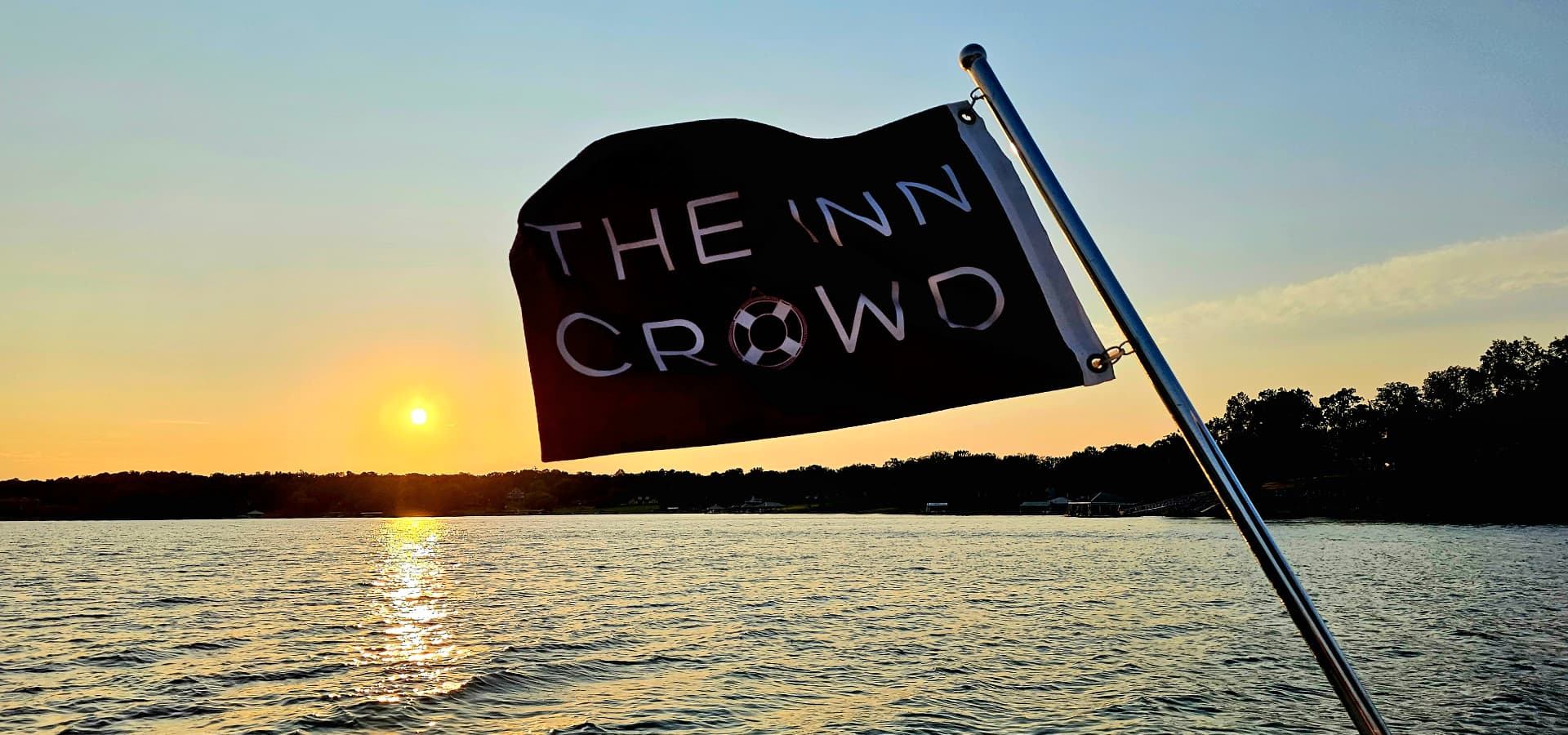 A black flag with "THE INN CROWD" and a soccer ball design waves over a shimmering lake at sunset.