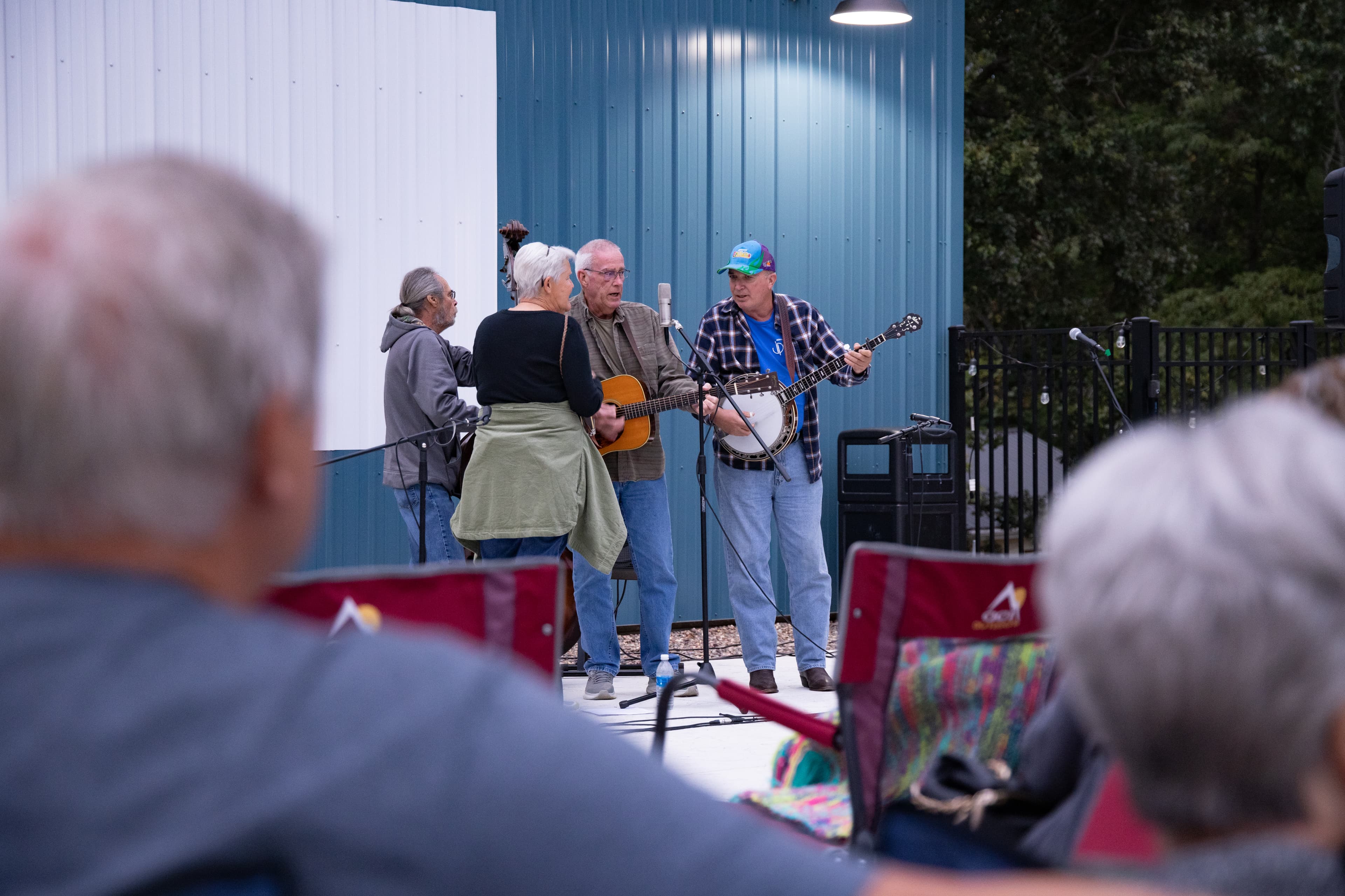 A group of musicians plays instruments while an audience sits in folding chairs.