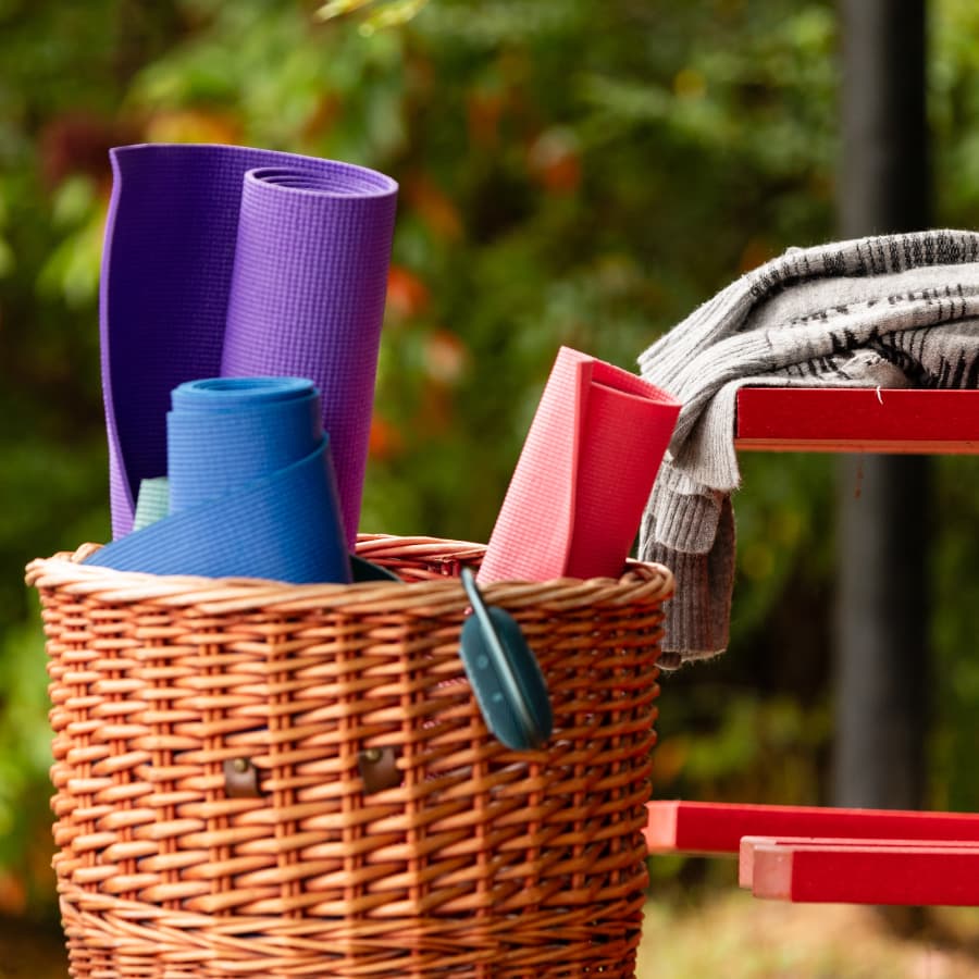 A wicker basket holds colorful yoga mats and a folded towel on a shelf outdoors.