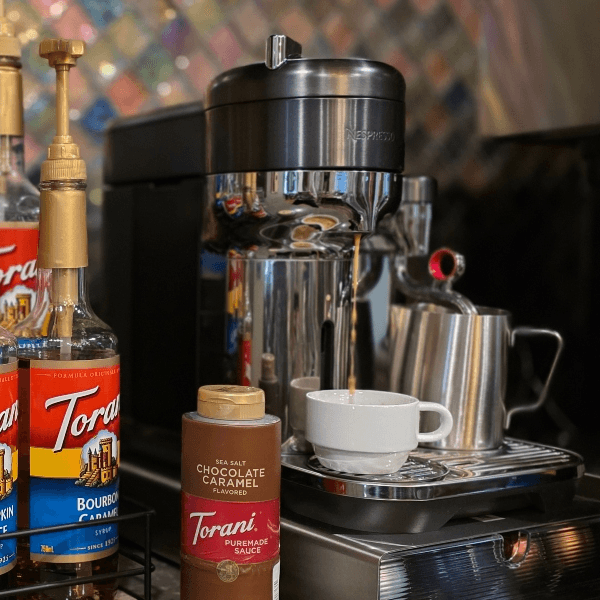 A coffee machine with various flavored syrups and a small cup on a countertop.