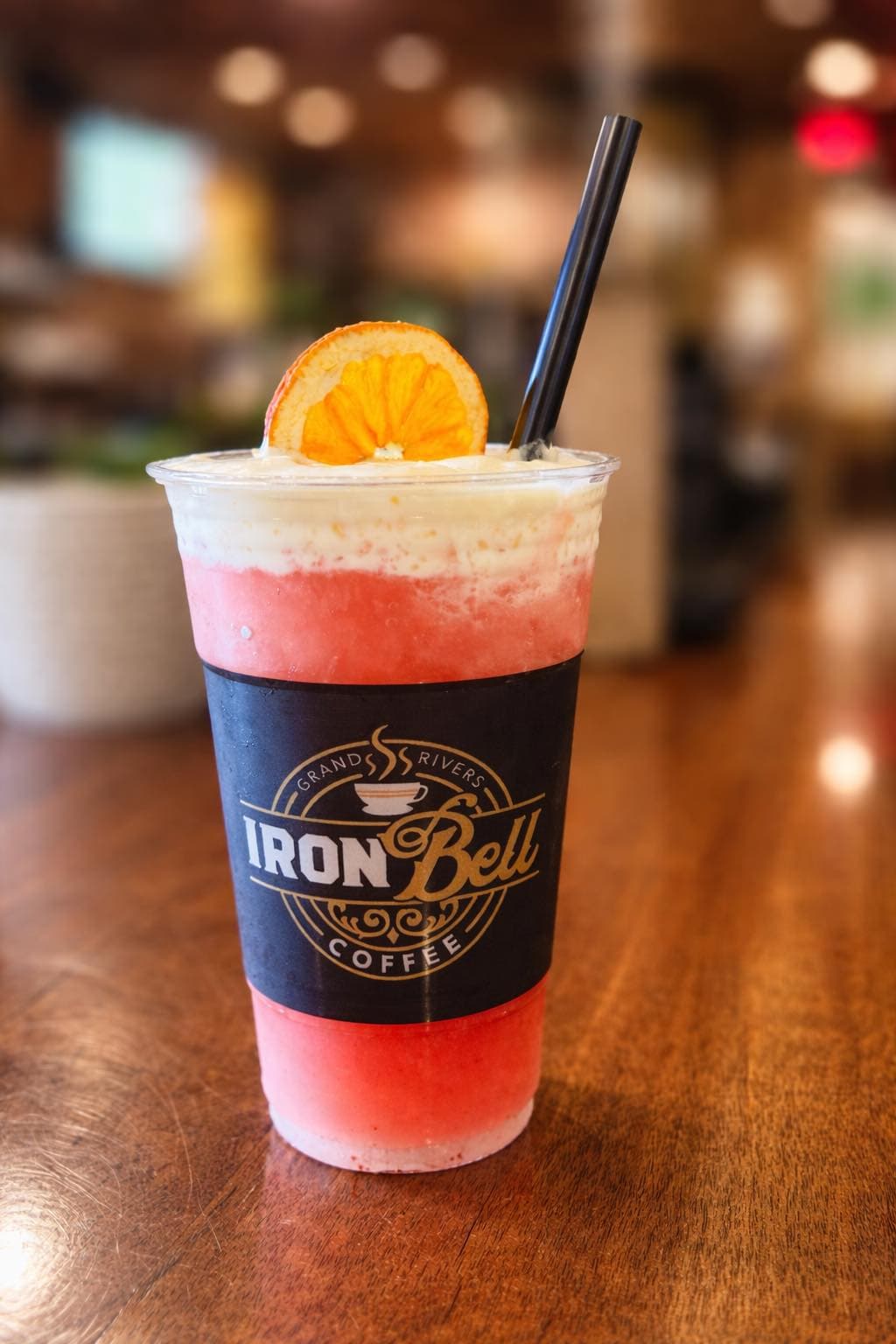 A frosty beverage with a slice of orange on top, served in a cup labeled "Iron Bell Coffee."